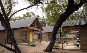 A wooden cabin with a covered patio area, surrounded by trees. - Lucky Arrow Retreat - Dripping Springs (Dripping Springs)