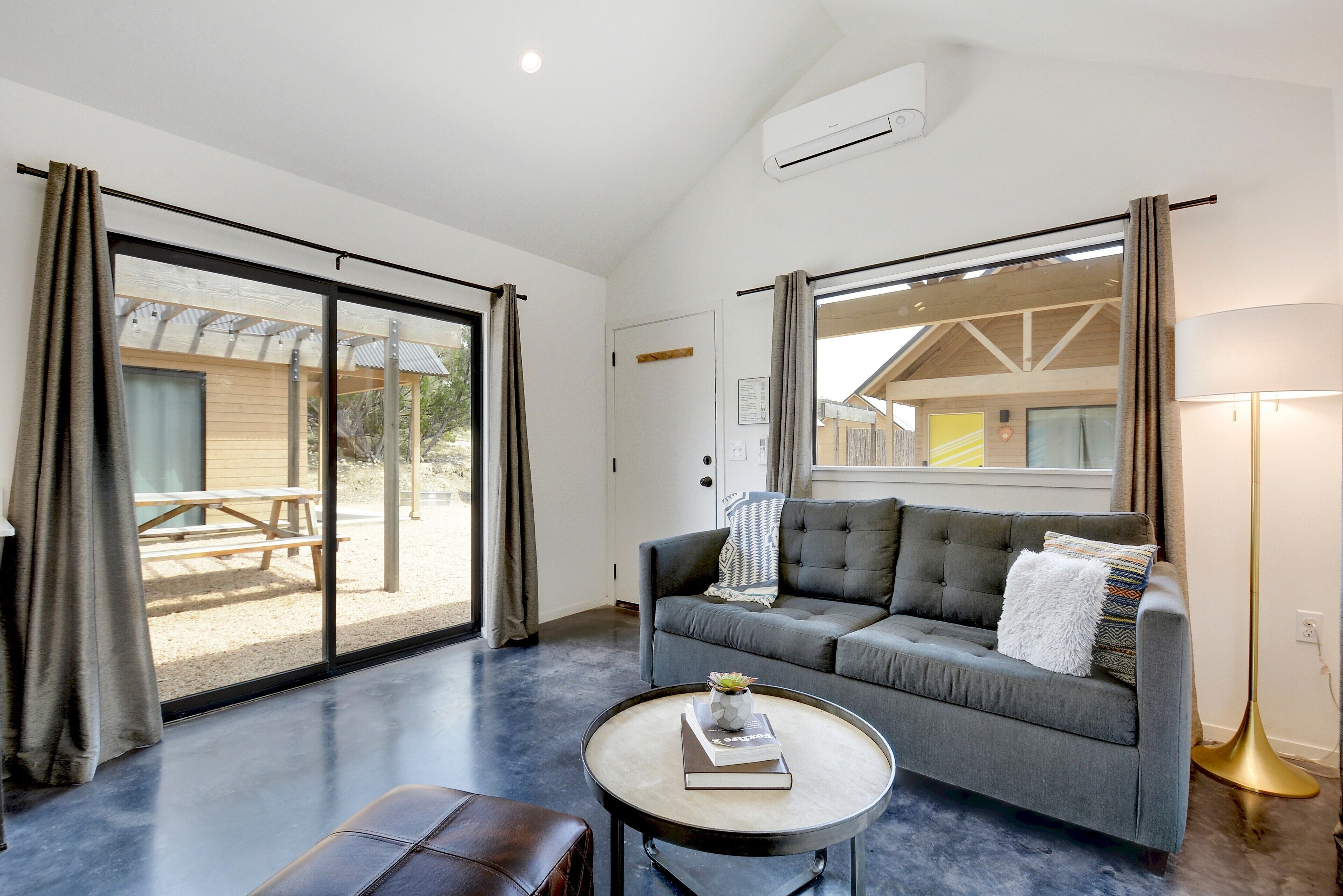 A modern living room with a grey sofa, a round coffee table, and a view of an outdoor patio.