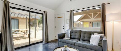 A modern living room with a grey sofa, a round coffee table, and a view of an outdoor patio.