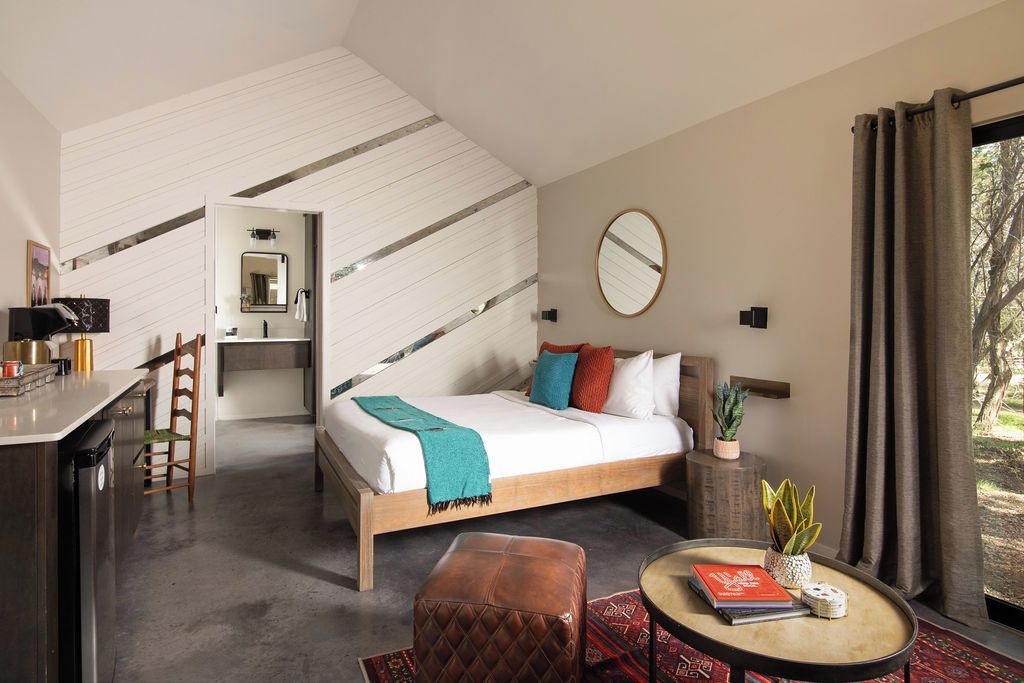 A modern bedroom with a bed, bedside table, and a view of the outdoors.