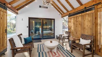 A cozy outdoor seating area with wooden furniture, a round table, and a view of a bedroom through glass doors.