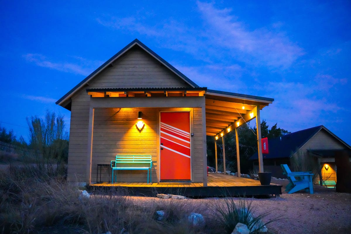 A wooden cabin with a covered porch, a bench, and a red door.