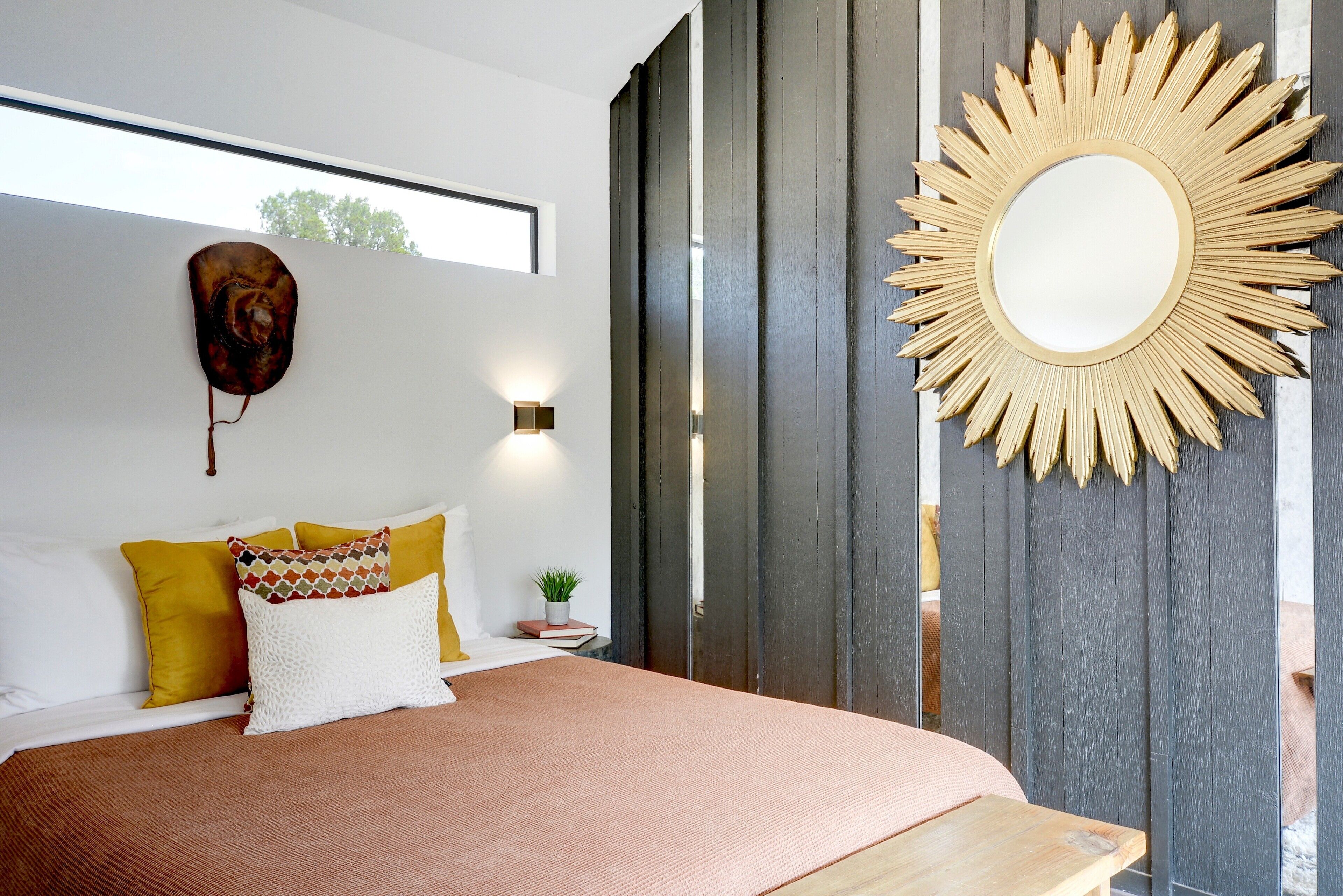 A modern bedroom with a large bed, a decorative wall mirror, and a small potted plant.