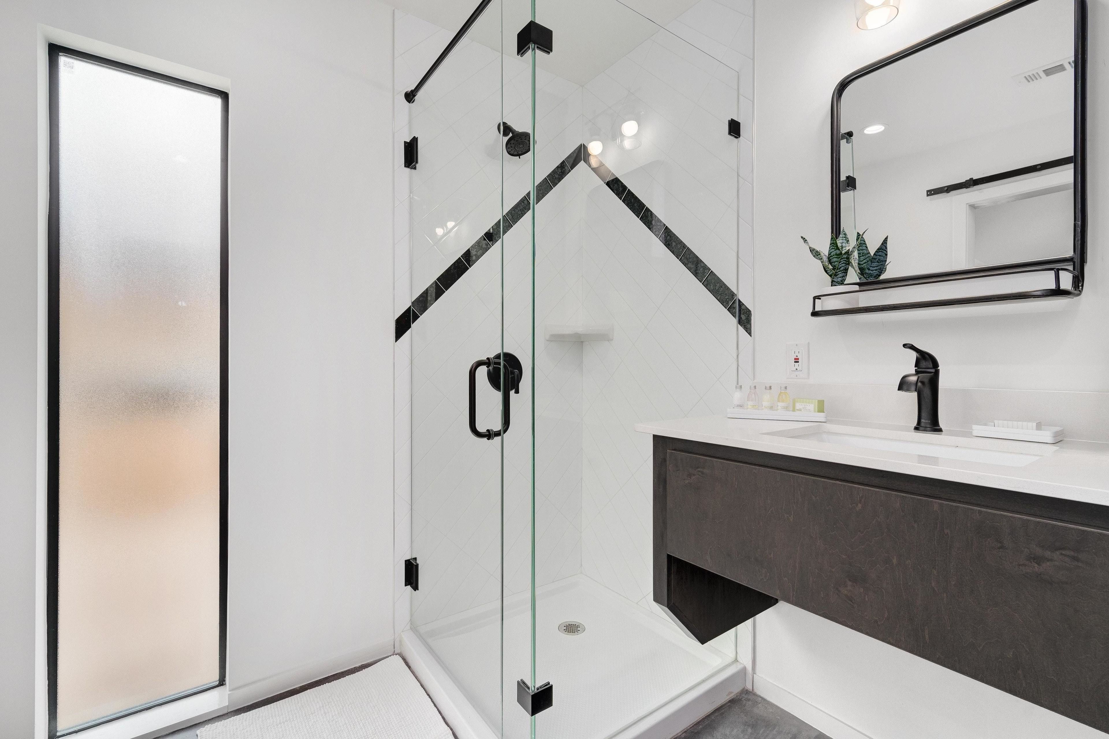 Ein modernes Badezimmer mit einer ein Glasfachwerk umschlossenen Dusche, einem dunklen Waschtisch und einem Spiegel über dem Waschbecken.
