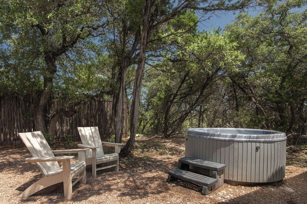 Two Adirondack chairs and a hot tub in a wooded area.