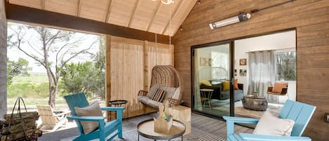 Una habitación amplia con paredes de madera, un gran ventanal corredero que da a un balcón y un ventilador de techo.