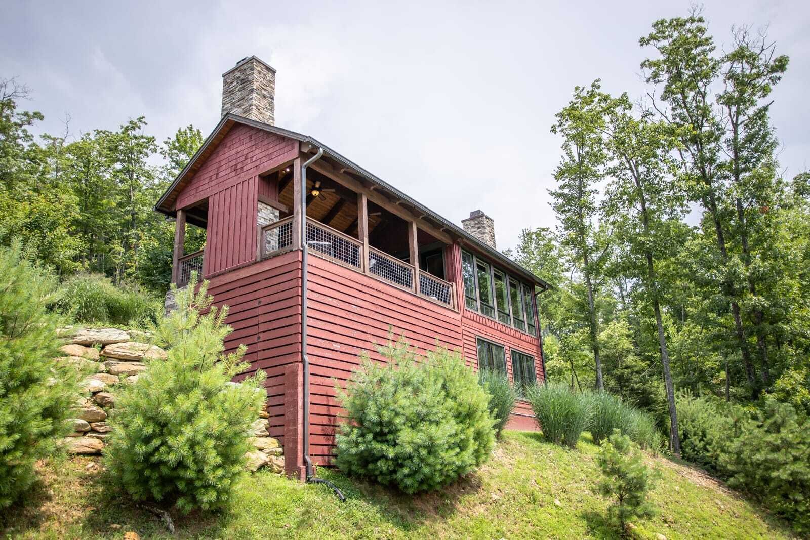A two-story wooden cabin with a balcony, surrounded by dense greenery and trees.