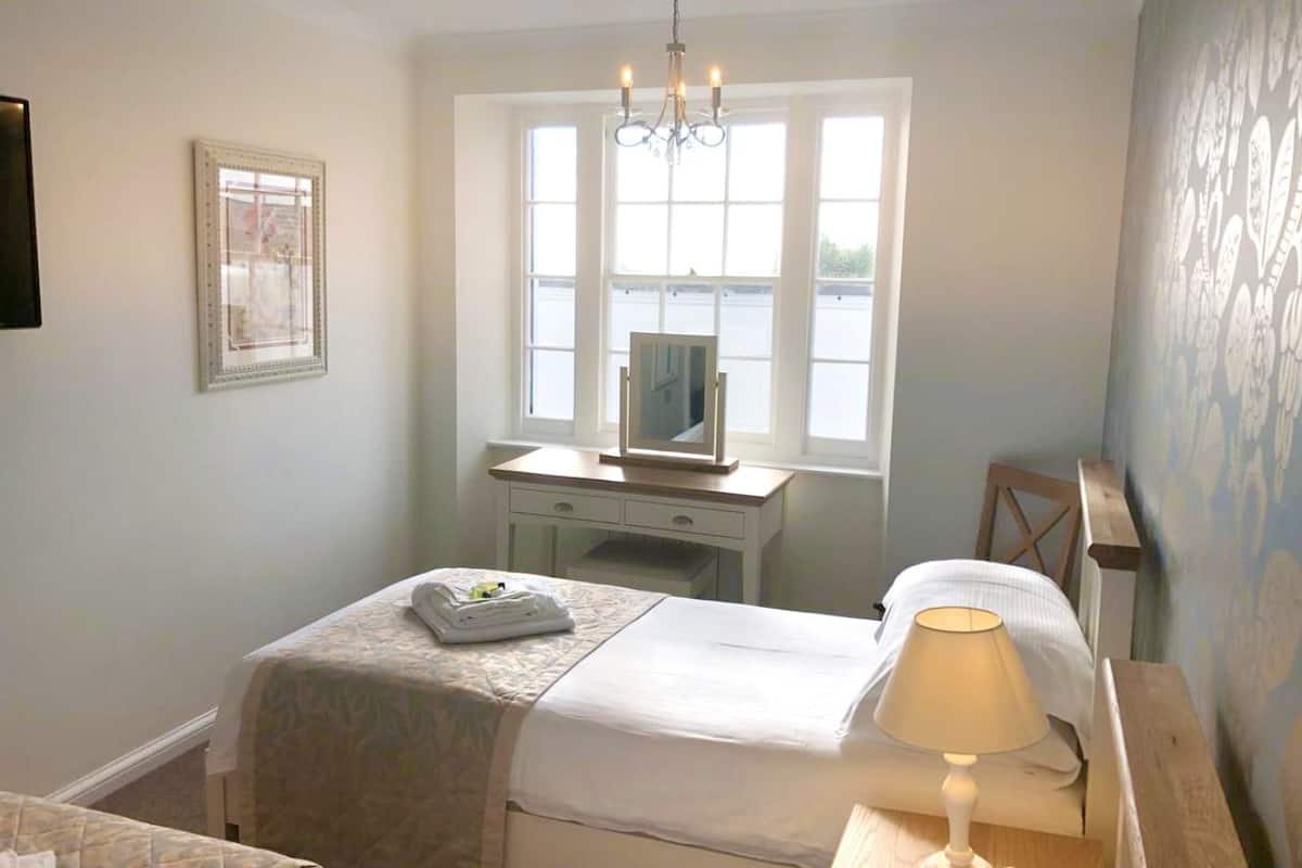 A bedroom with a bed, bedside table with a lamp, a dresser, and a window.