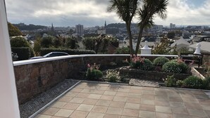 Una terraza en la azotea con muros de piedra, suelo de baldosas y vistas a un paisaje urbano.