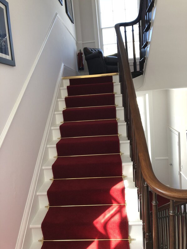 A staircase with a red carpet and white walls, leading to a door at the top. - Almorah hotel (St. Helier)