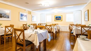 Un comedor con varias mesas, sillas de madera y cuadros en las paredes.