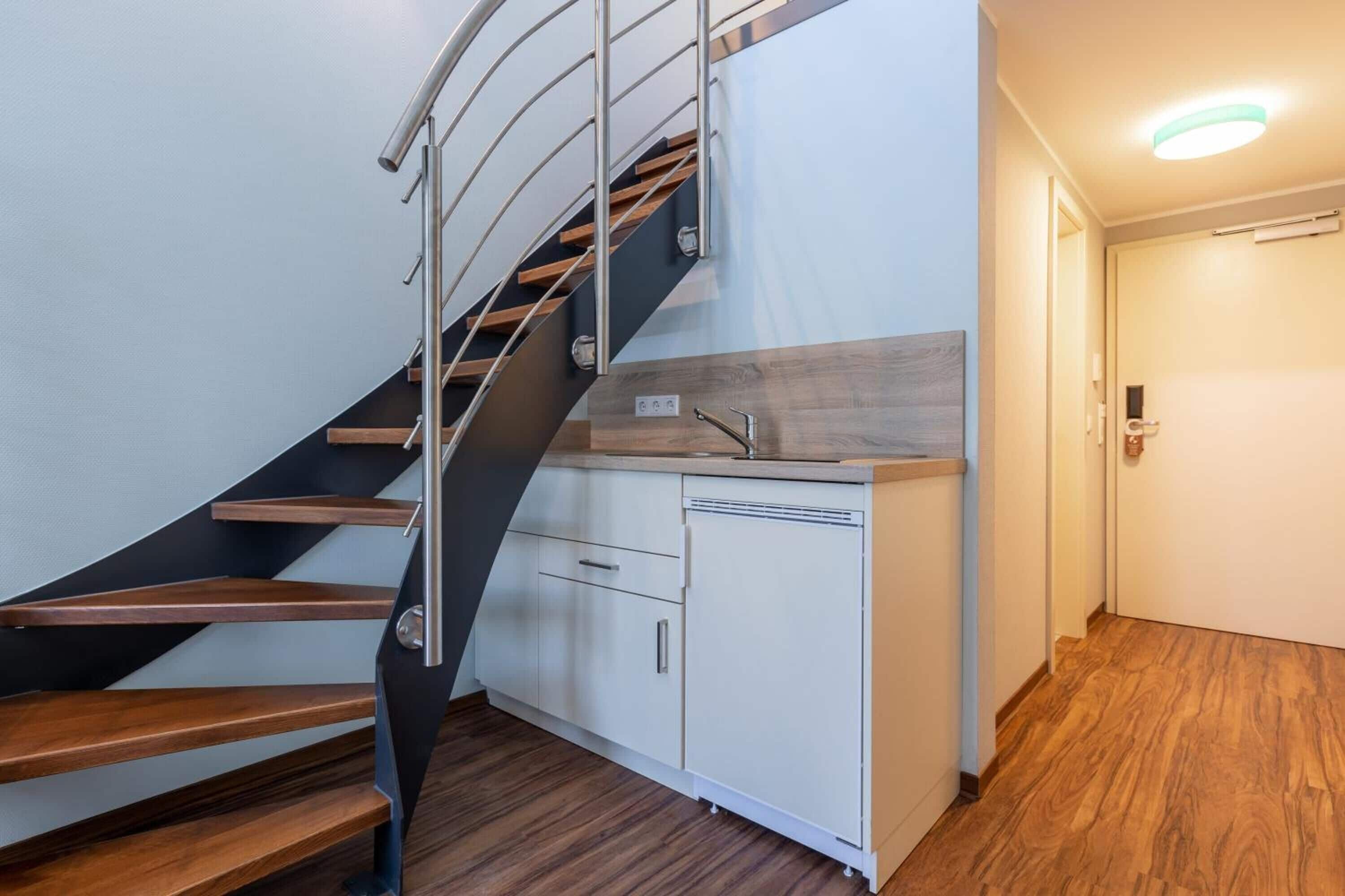 A modern kitchen with a wooden countertop and white cabinets, a built-in dishwasher, and a stainless steel staircase.