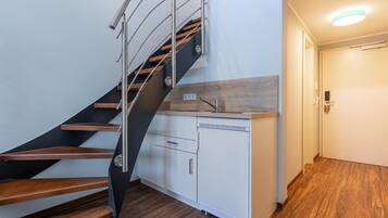 A modern kitchen with a wooden countertop and white cabinets, a built-in dishwasher, and a stainless steel staircase.