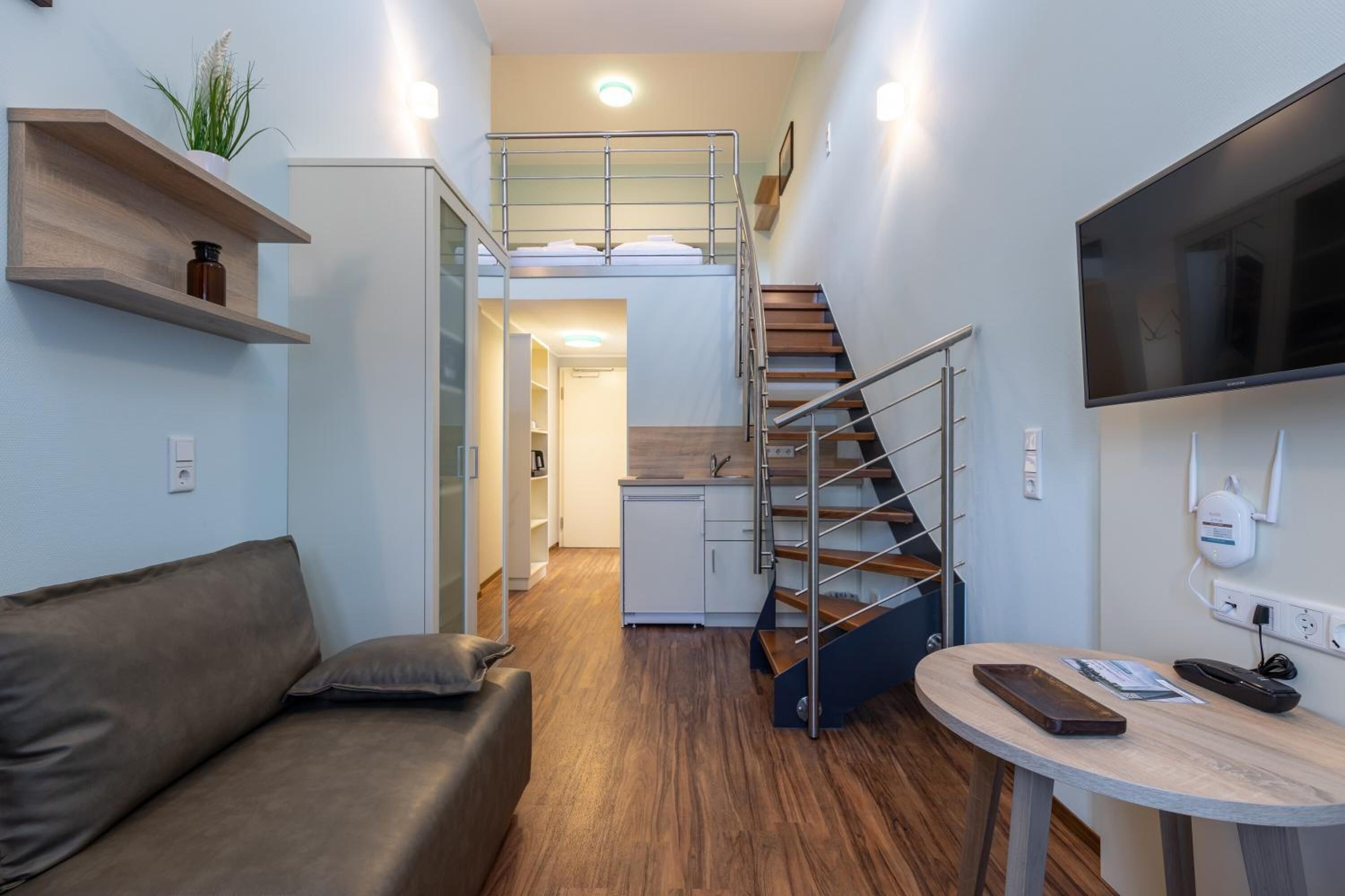 Un espacio habitable compacto con sofá, una mesita, televisor, escalera y una kitchenette.