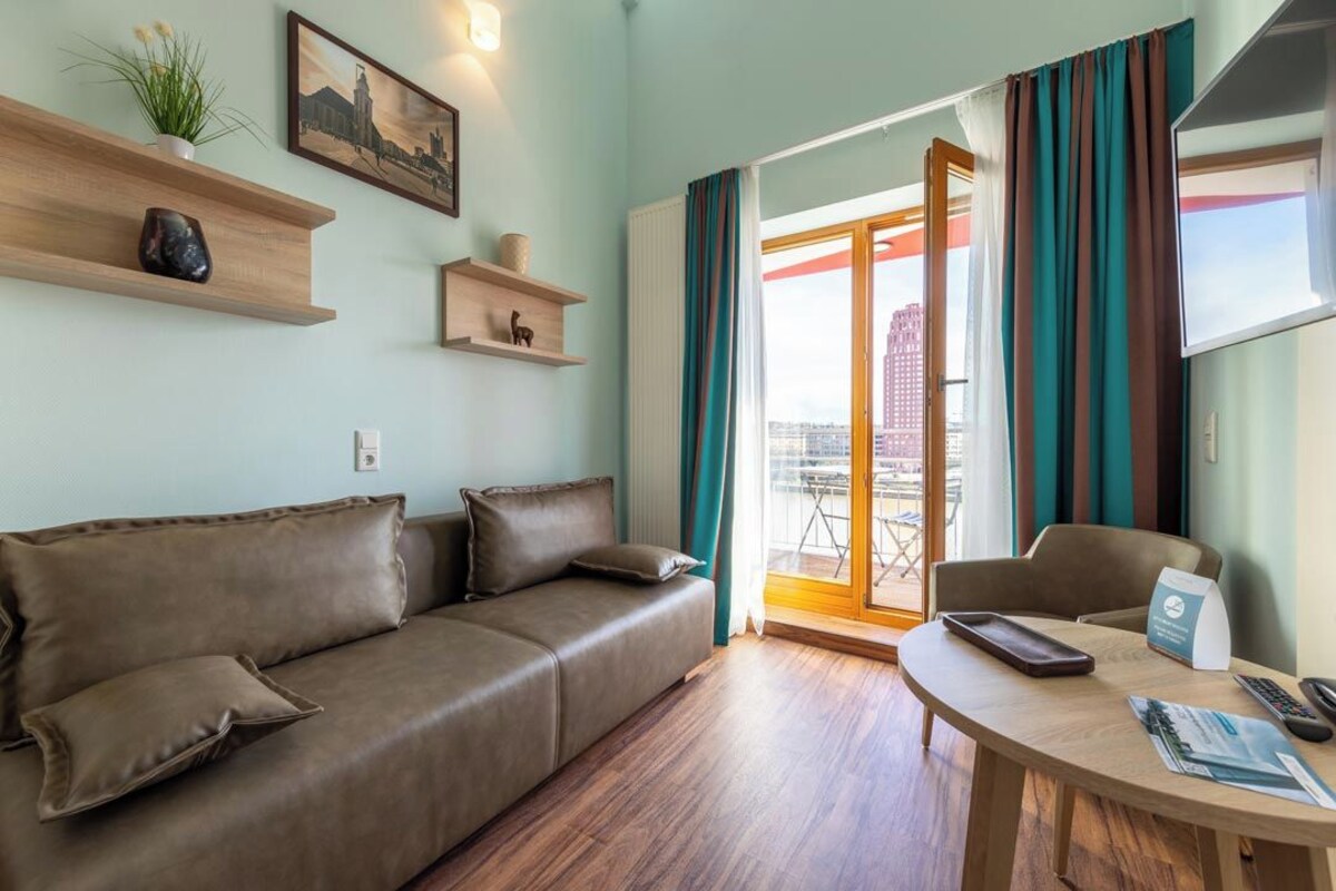 A modern living room with a brown leather sofa, a wooden coffee table, and a city view through a glass door.