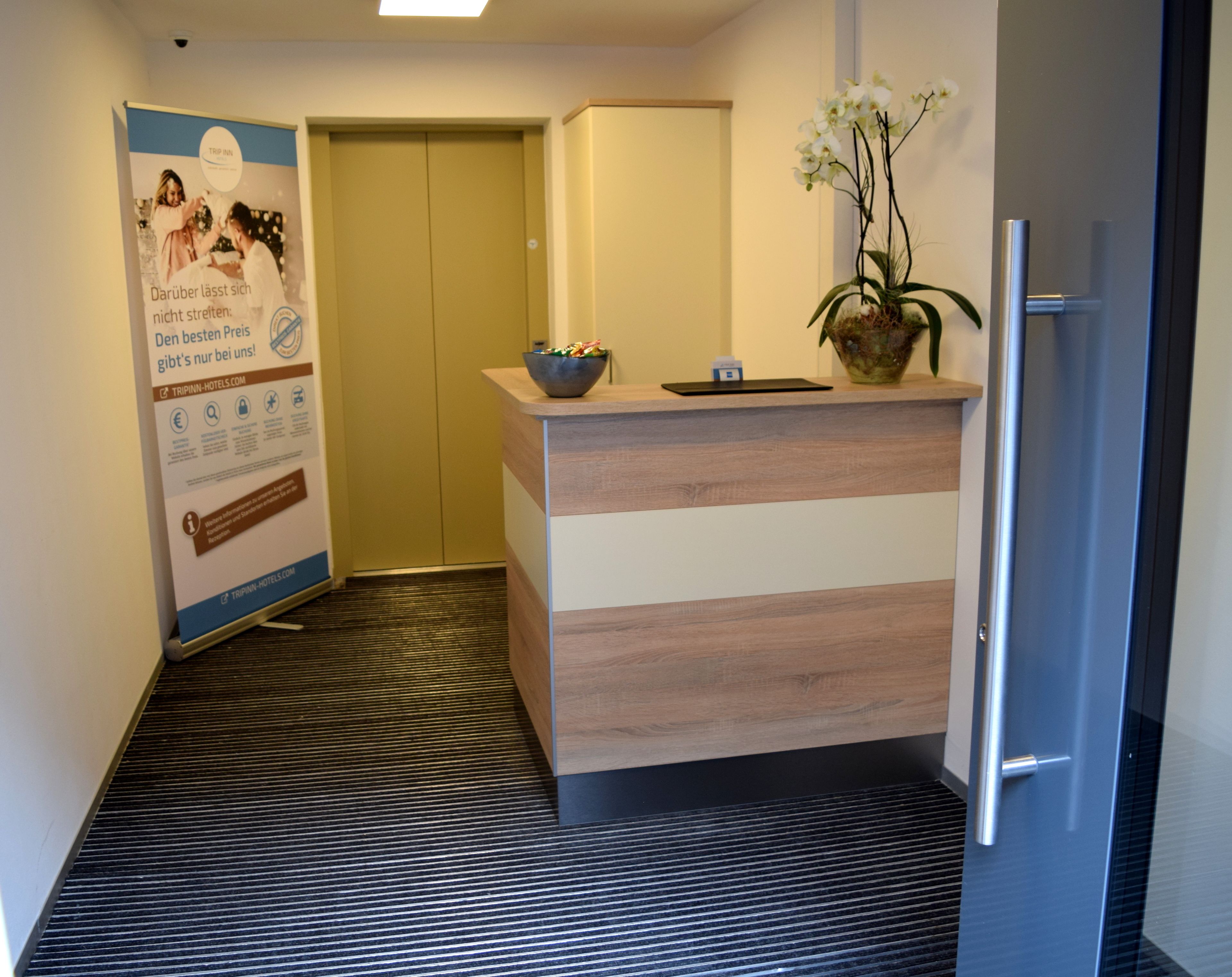 A reception desk with a plant, a poster, and a door in a hotel lobby.
