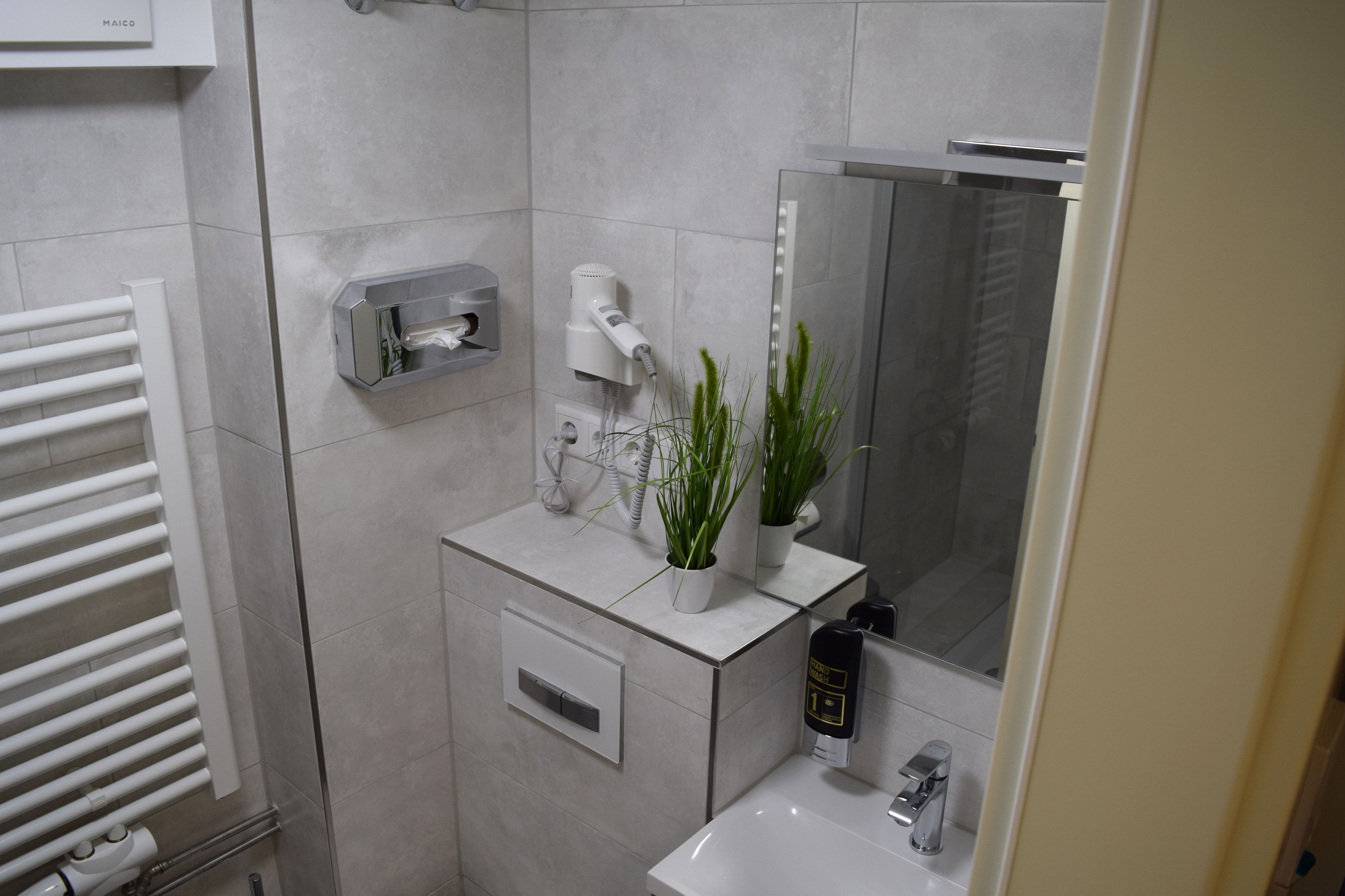 A modern bathroom with a white sink, a mirror, a towel rack, a hairdryer, and a small potted plant.