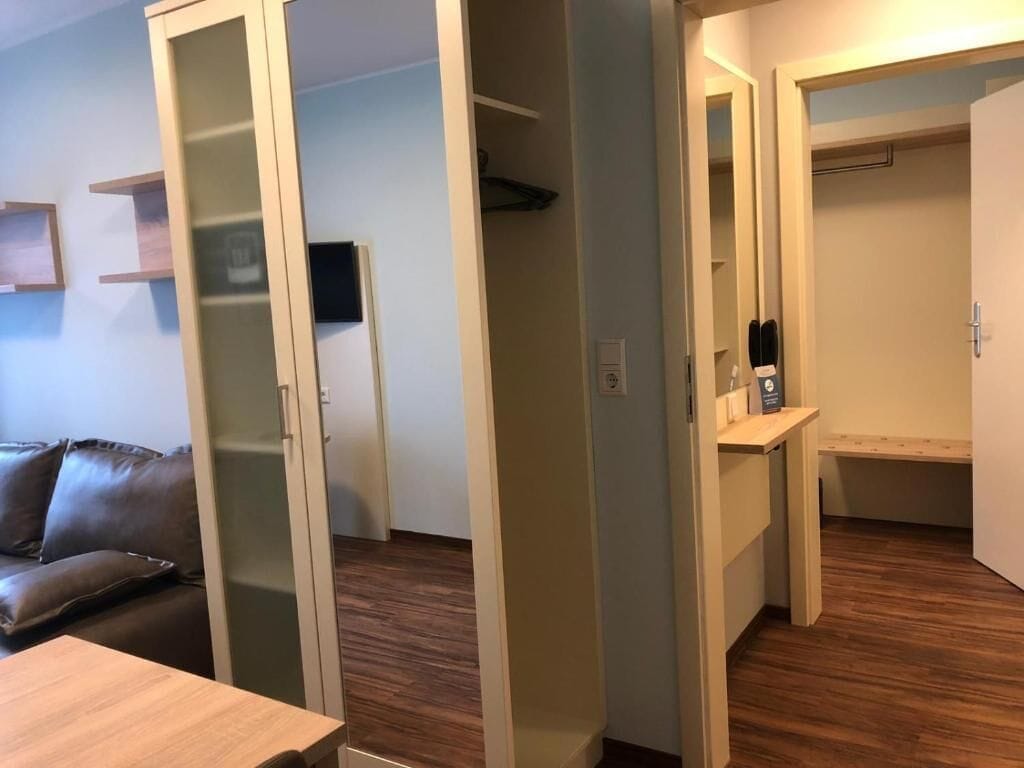 Una habitación con piso de madera, un sofá de cuero marrón, una mesa de madera y un armario con espejo.