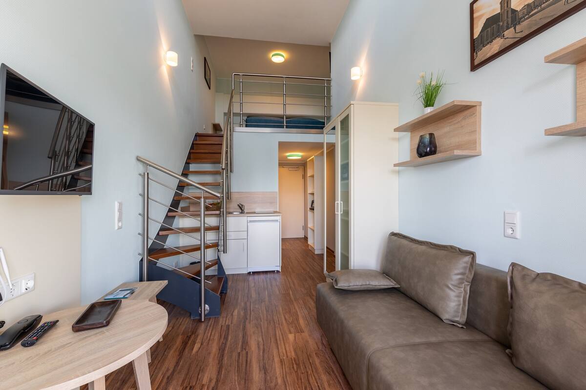 A compact living space with a bunk bed, a kitchenette, a dining area, and a sofa.