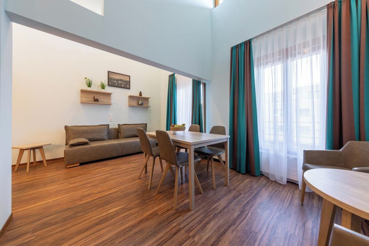 A modern living room with a sofa, dining table, chairs, and a small coffee table. There are two wall-mounted shelves with decorative items.