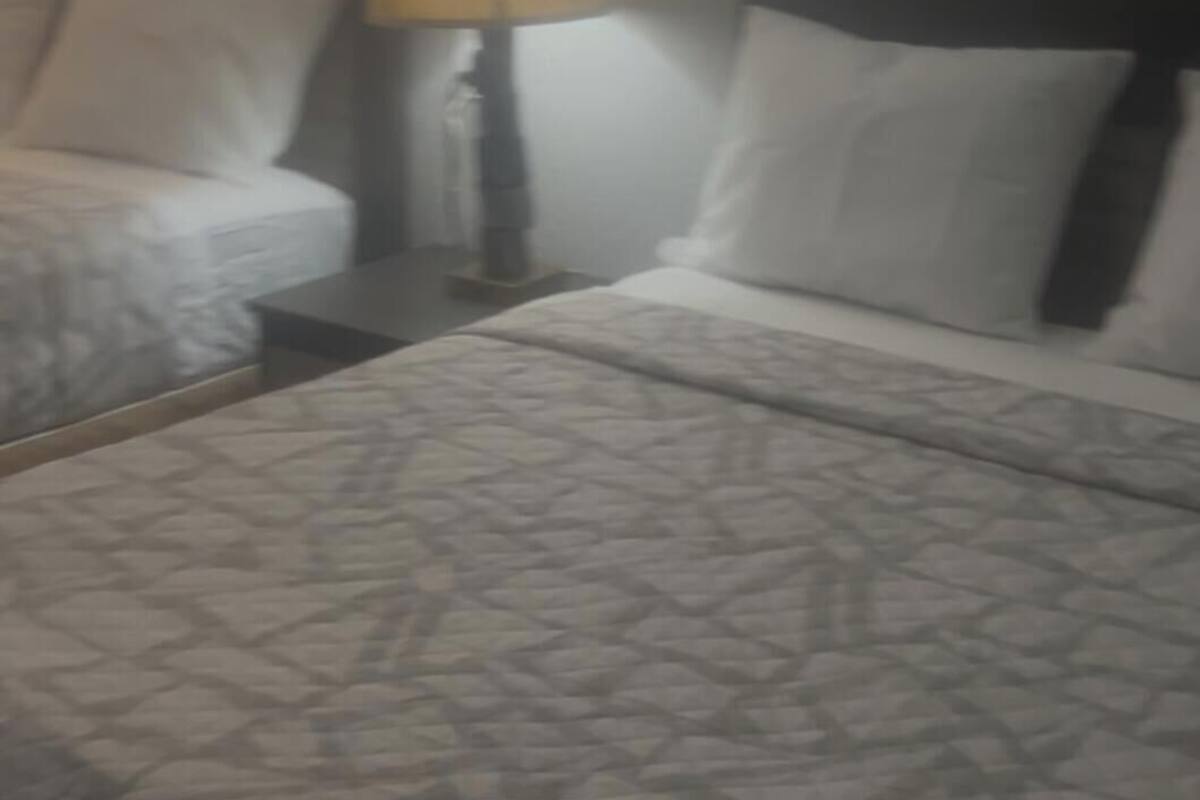 A hotel room with two beds, a nightstand with a lamp, and a notepad on the bed.