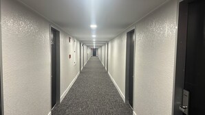 A long, narrow hotel corridor with carpeted floors, doors on both sides, and a ceiling light. - Regency Inn (Perry)