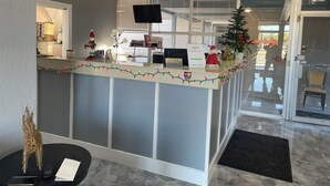 A reception desk with a Christmas tree, a small Christmas ornament, and a sign indicating a 24-hour check-in service. - Regency Inn (Perry)