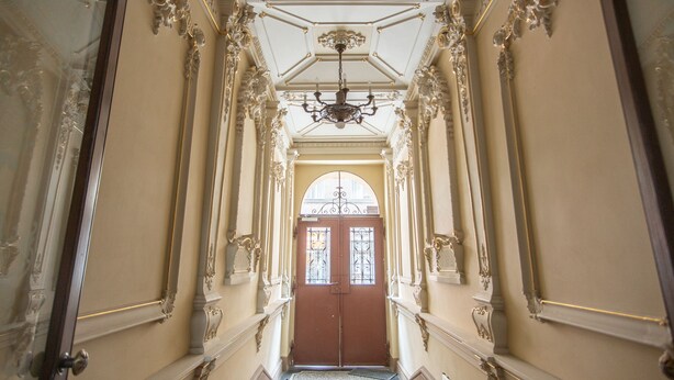 A grand hallway with ornate columns, a chandelier, and a red door at the end. - Luxurious 5-bedroom apartment with wellness amenities (Prague)