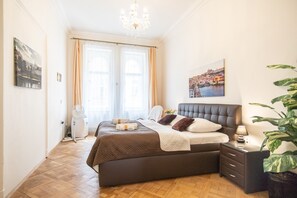 Une chambre avec un grand lit, une table de chevet, un ventilateur et une plante en pot.