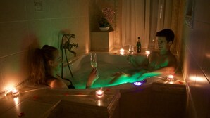 A couple in a dimly lit, green-hued bathtub with candles, suggesting a romantic setting. - Luxurious 5-bedroom apartment with wellness amenities (Prague)