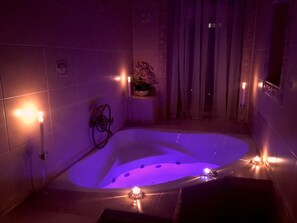 Une salle de bain moderne à la lumière tamisée, avec une baignoire sur pieds, un espace douche et une plante en pot posée sur une petite table.