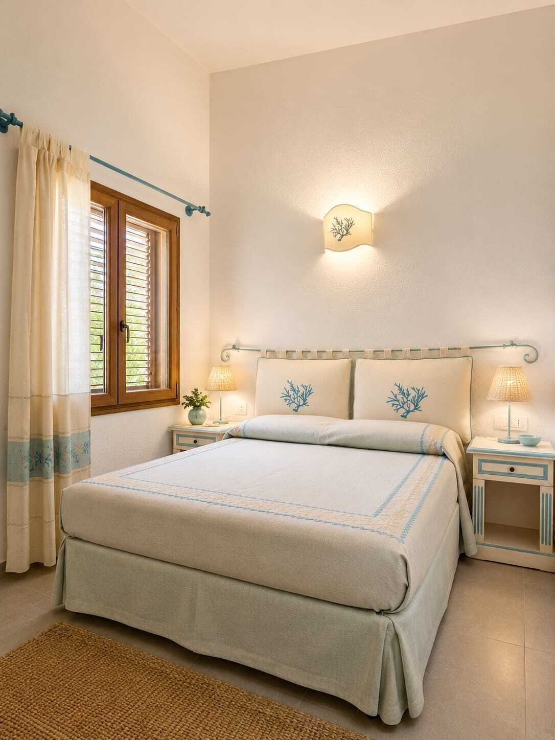 Ein Schlafzimmer mit Bett, Nachttischen, einem Fenster mit Vorhängen und einer Wandleuchte.