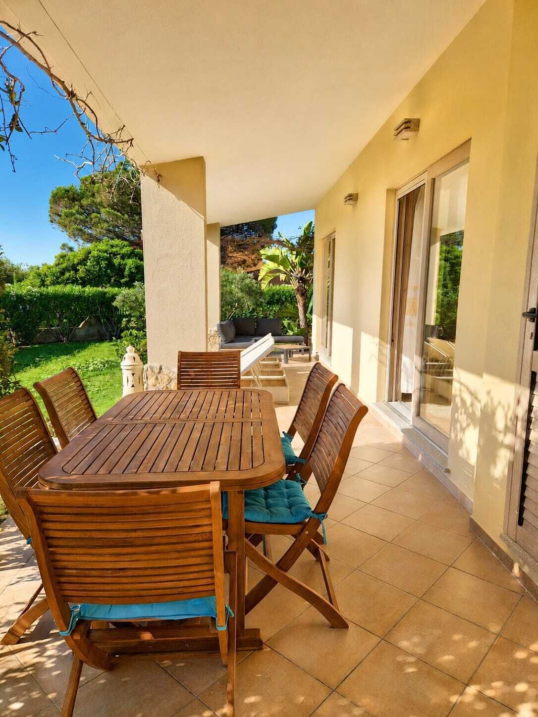 Eine überdachte Terrasse mit Holztisch und -stühlen, einer Sitzecke und Blick auf einen üppigen Garten.