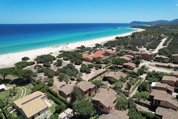 Vista aérea de una zona costera con playa, villas y un mar azul cristalino.
