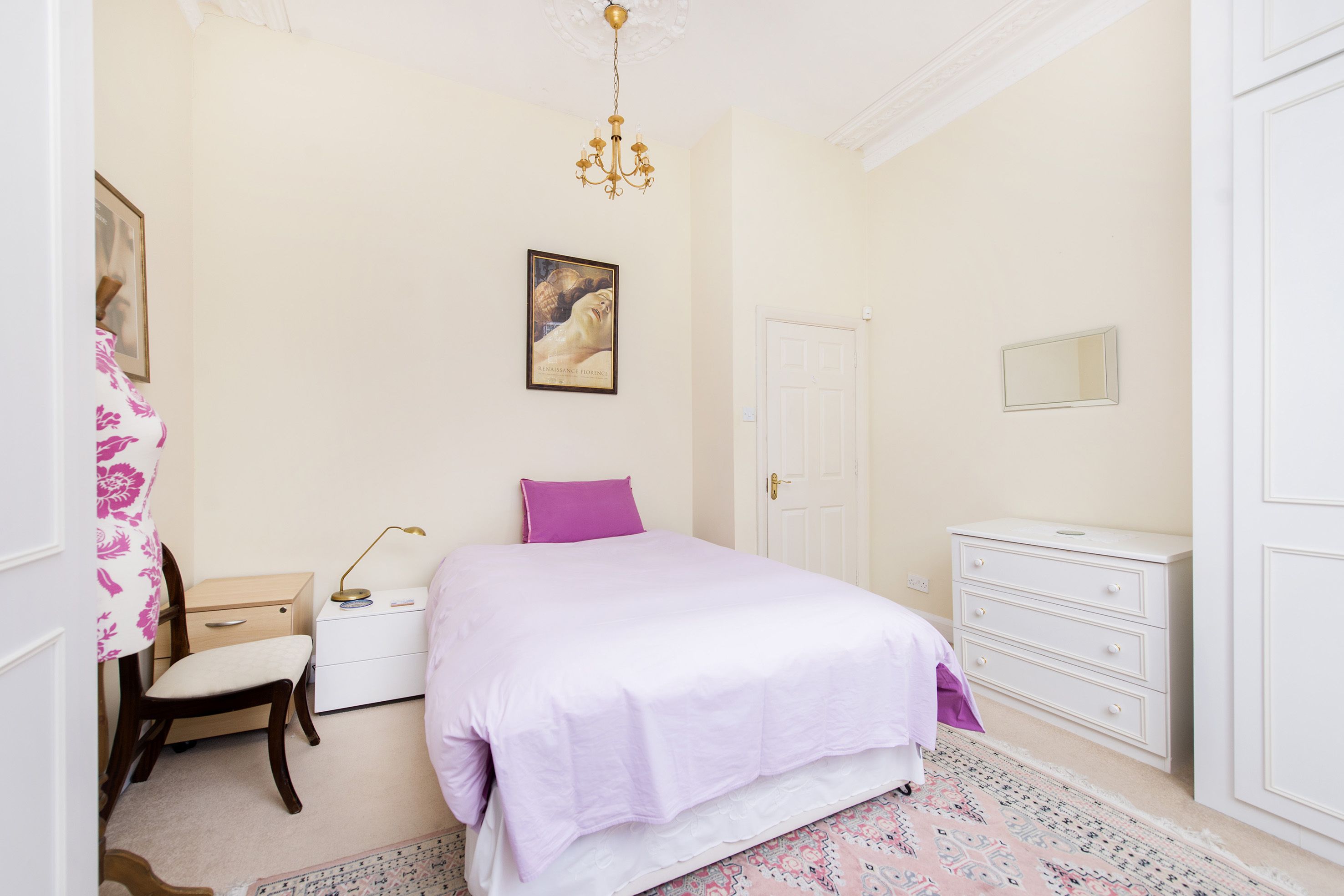 A bedroom with a bed, a nightstand, a chair, a dresser, a door, and a chandelier.