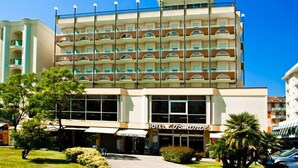 Un hotel de varios pisos con una entrada central, balcones en cada planta y un cielo despejado.
