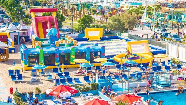 Un resort frente al mar con estructuras hinchables para jugar, sillas de sol y una piscina.
