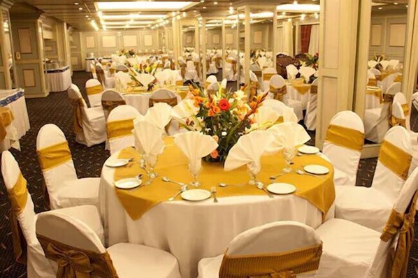 A banquet hall with round tables set for a formal event, each with white tablecloths and gold sashes on the chairs.