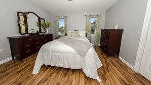 Een slaapkamer met een groot bed, twee nachtkastjes, een spiegel en een raam met gordijnen.