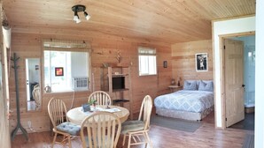 A wooden cabin with a round dining table, two chairs, a bed, and a television. - Cozy Cabin in Kettle Valley (Rock Creek)