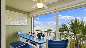 Een balkon met een tafel en stoelen, een plafondventilator en uitzicht op de oceaan.