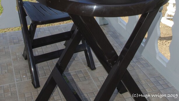 Una mesa redonda con platos, tazones y una jarrón blancos, ubicada en un balcón con vistas al mar.