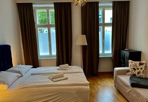 A hotel room with a large bed, a sofa, a lamp, and a view of the outdoors through the window.