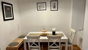 Un comedor con una mesa blanca, cuatro sillas blancas, un banco y cuadros en la pared.