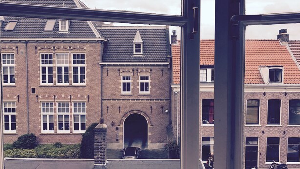 A traditional brick building with multiple windows and a central archway, viewed through a window frame.
