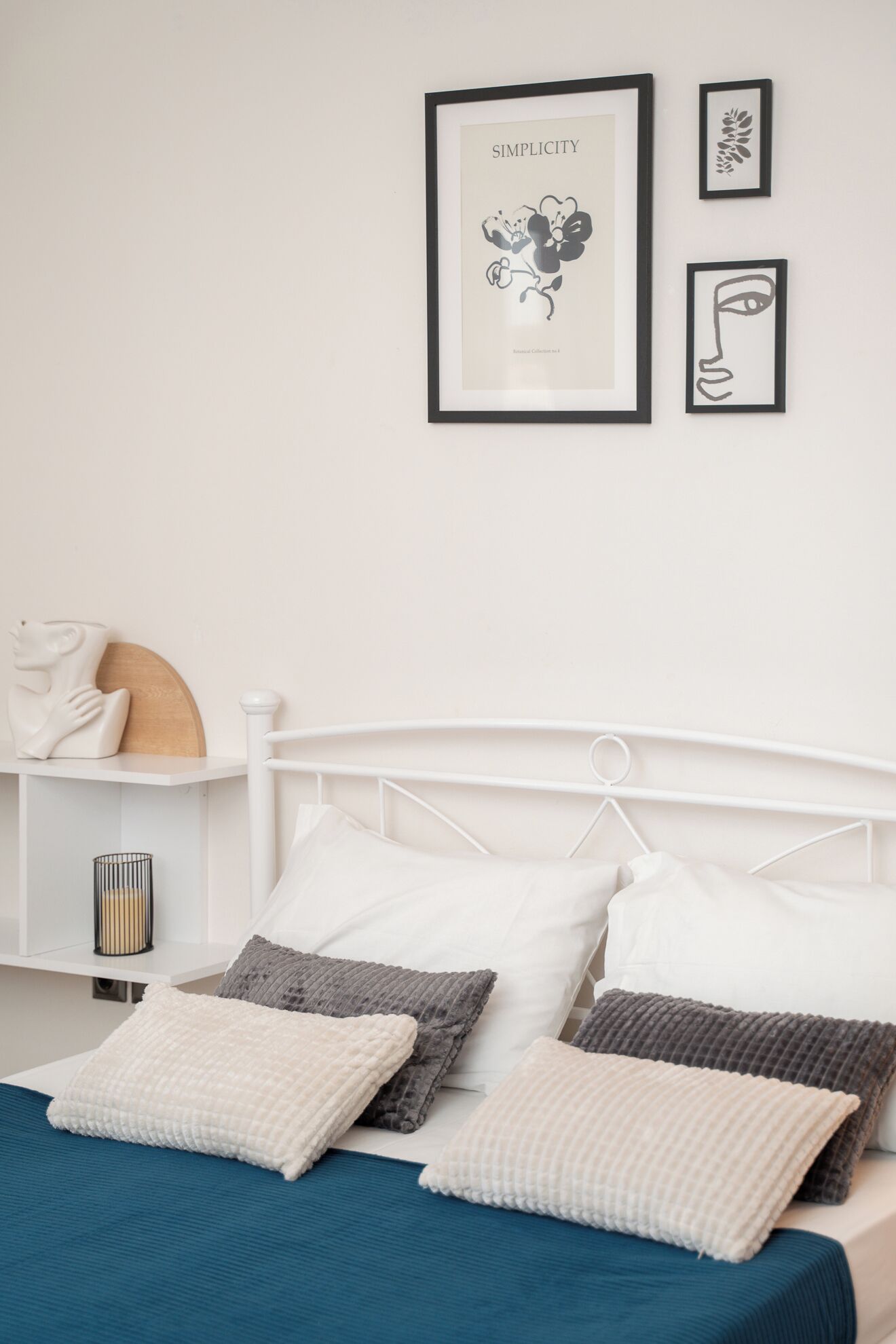 Una camera da letto con un letto bianco, numerosi cuscini, una coperta blu e una parete decorata con opere d'arte.