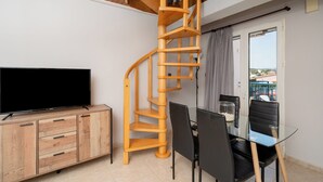 Un espacio habitable compacto con una escalera espiral de madera, un televisor de pantalla plana, un mueble de madera, una mesa de comedor con sillas y una mesa de vidrio.