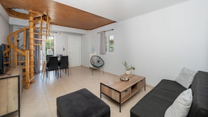 Amplia sala de estar con una escalera espiral de madera, una mesa de comedor con sillas, un sofá y una mesa de centro.