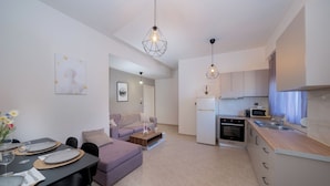 Un apartamento moderno con comedor, sala de estar con sofá, cocina equipada con microondas y horno, y luces colgantes.
