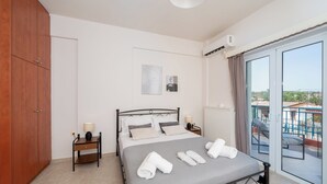 Un dormitorio con cama, armario, mesita de noche, lámpara y vista a un balcón.